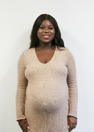 Sandra Igwe, a Black woman with long black hair and a baby bump, wearing a long cream dress